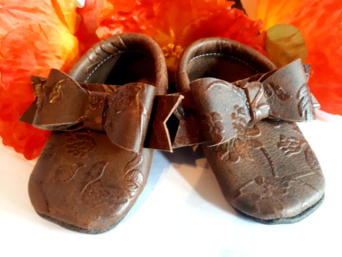 Floral embossed brown leather moccs with short fringe and bows